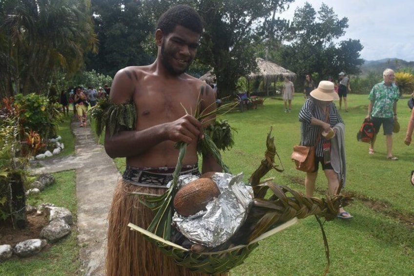 A person carrying a coconut and a plant in a tropical garden setting. 5