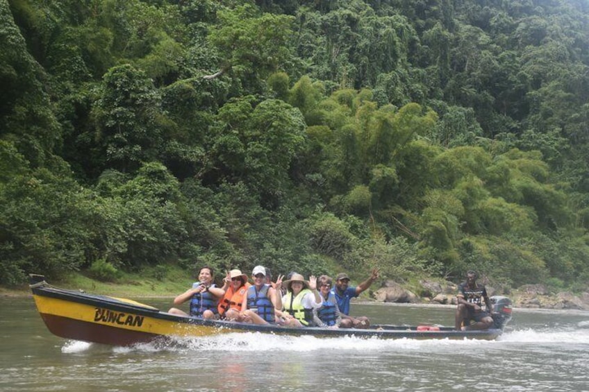 A group of people in a yellow boat labeled 'BUNCAN' on a river surrounded by dense green forest. 4