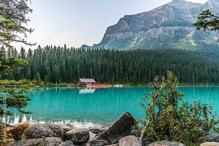 A turquoise lake with a cabin, surrounded by dense forest and mountains. 2