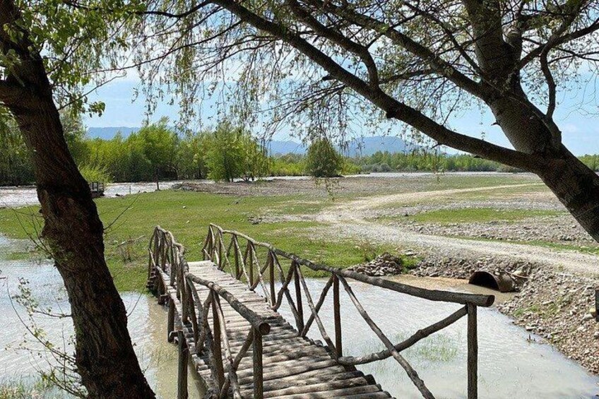 Un pont en bois enjambe une rivière, bordée d’arbres de chaque côté. 2
