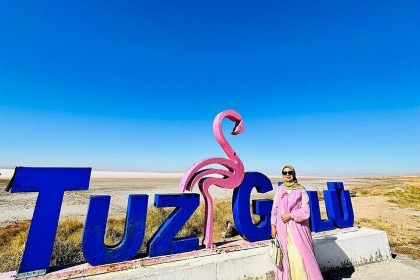 A person standing in front of a sign with the text 'Tuz Gut' and a pink flamingo sculpture. 4