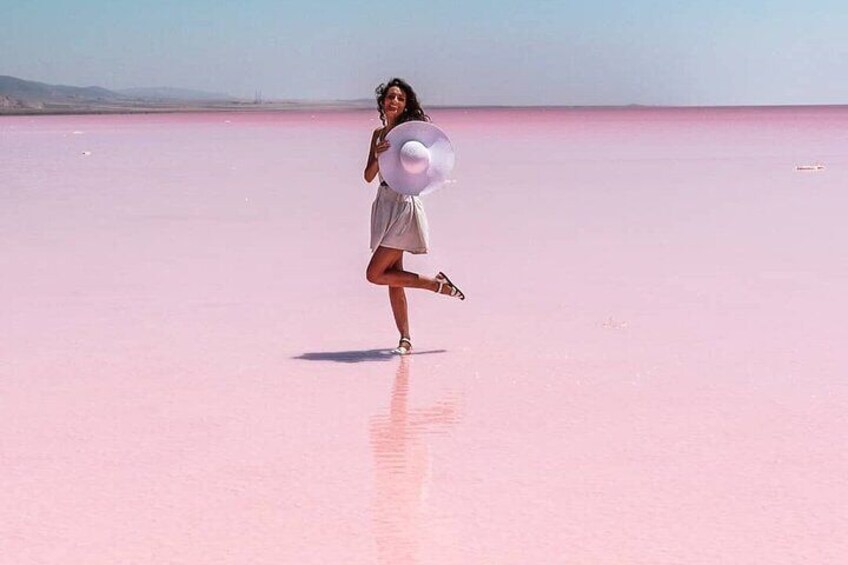 A person in a white dress standing on a pink salt flat with a white hat. 5
