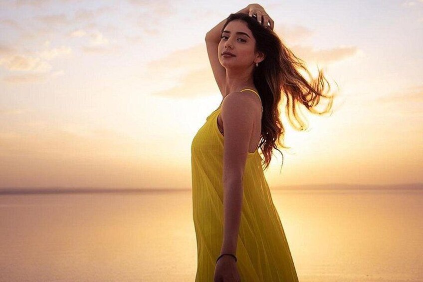 A person in a yellow dress standing on a beach with a sunset in the background. 2