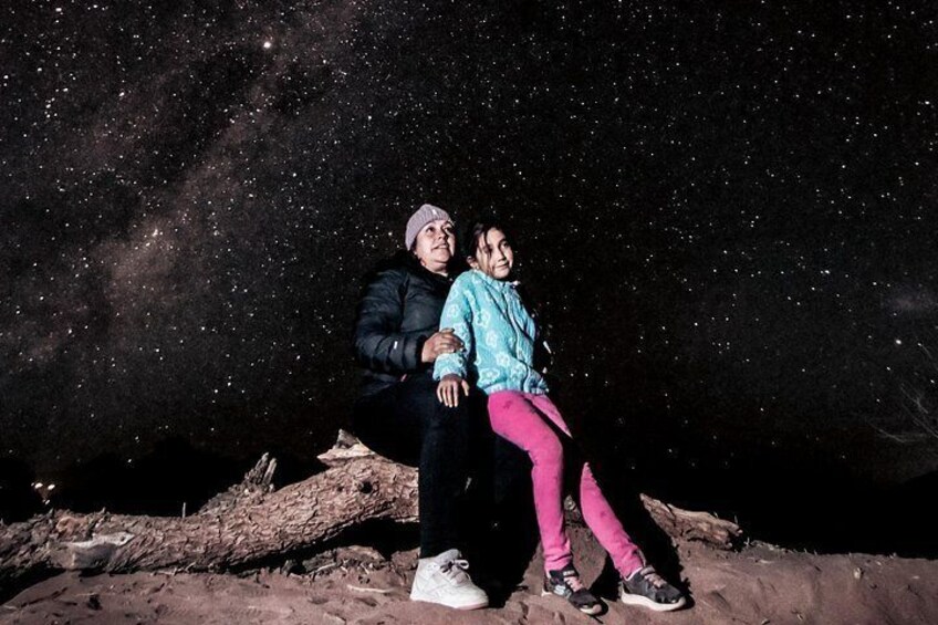 Two people sitting on a log under a starry night sky. 1