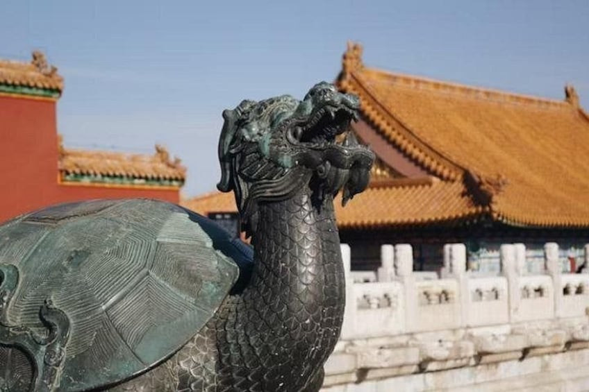 A bronze statue of a dragon with a detailed scale pattern, set against a traditional Chinese building with ornate roof tiles. 1