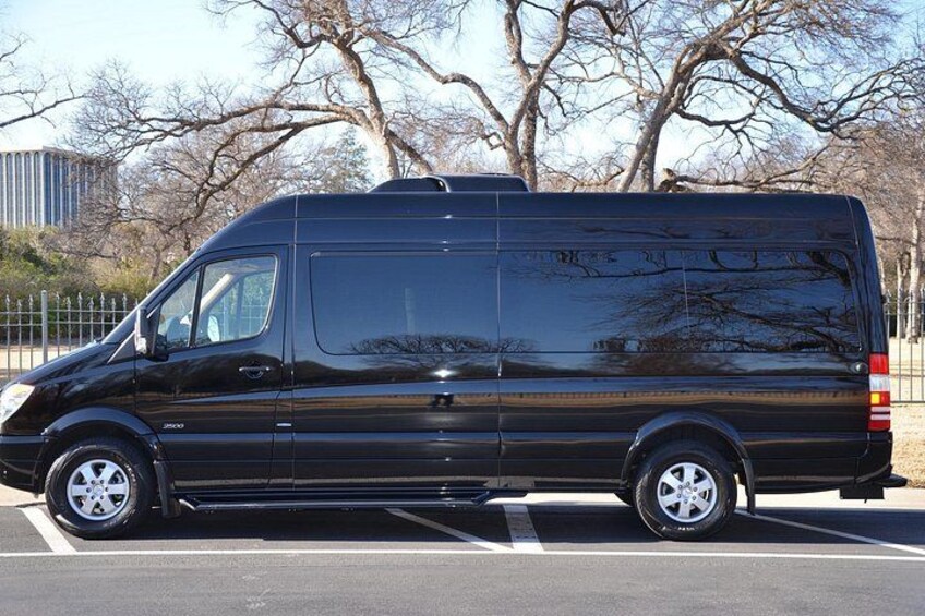 A black van parked in a parking lot with trees and a building in the background. 1