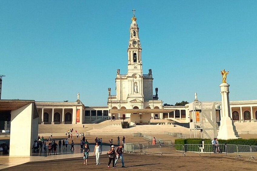 A large cathedral with a tall bell tower, a statue, and a plaza with people walking. 1