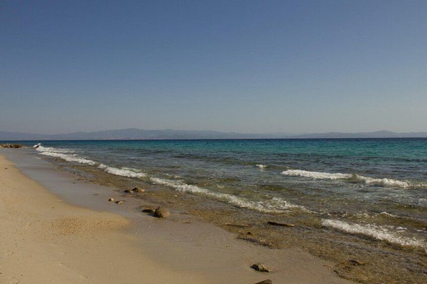 A beach with clear blue water, a sandy shore, and distant mountains. 3