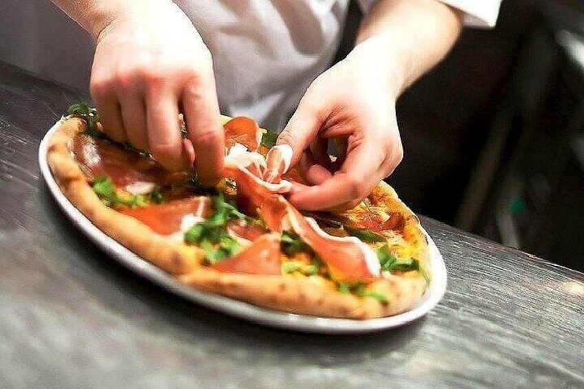En person lægger skiver af kød på en pizza. 3