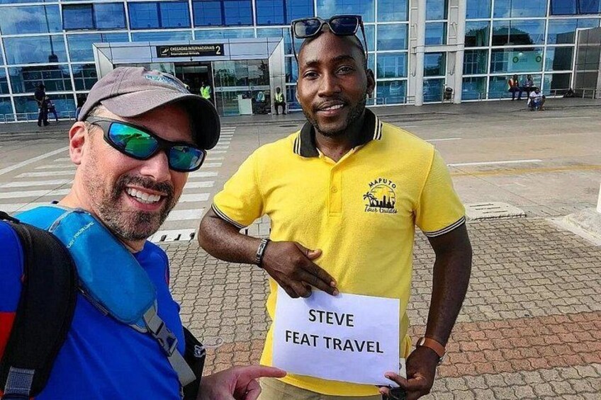 Two people standing in front of a building with a sign that reads 'Steve Feat Travel'. 1
