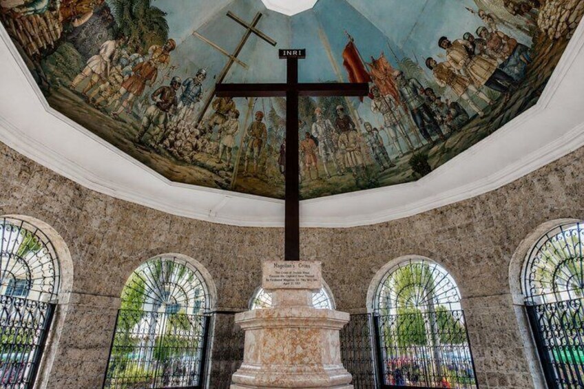 A church interior with a large cross, stained glass windows, and a mural on the ceiling. 1