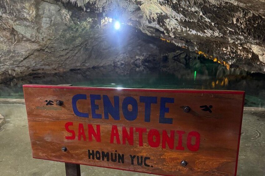 Een houten bord met daarop de tekst 'CENOTE SAN ANTONIO' en 'HOMUN YUC'. 4