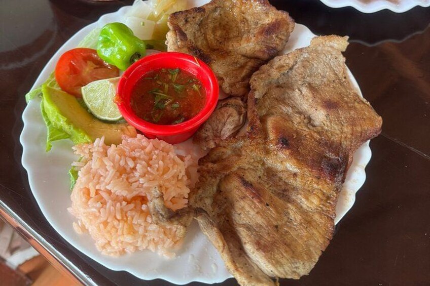 Een bord met gegrild vlees, rijst, avocado, tomaat, limoen en rode saus. 2