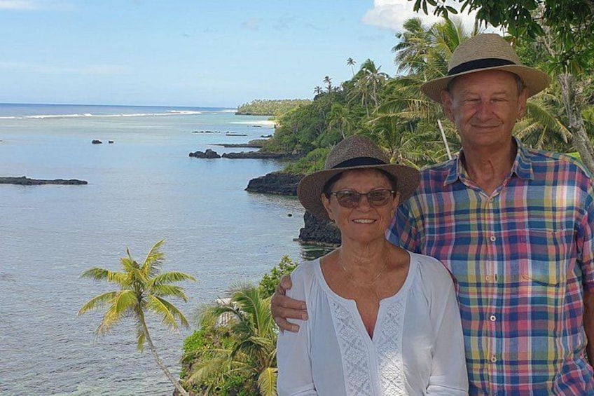 Two people standing by a coastal area with palm trees and a view of the ocean. 4