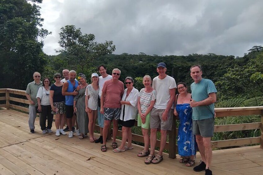 Un groupe de personnes se tient sur une terrasse en bois, avec un paysage boisé en arrière-plan. 3