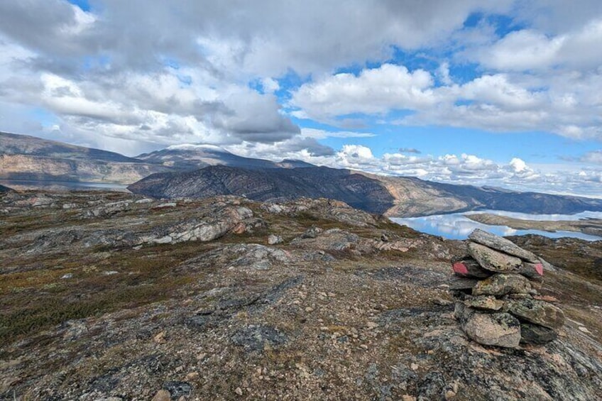 A rocky landscape with a stack of stones, a lake, and distant mountains under a partly cloudy sky. 4