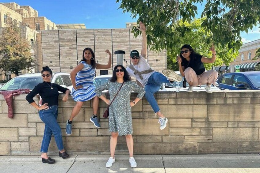 A group of people posing on a stone wall with cars parked in the background. 2