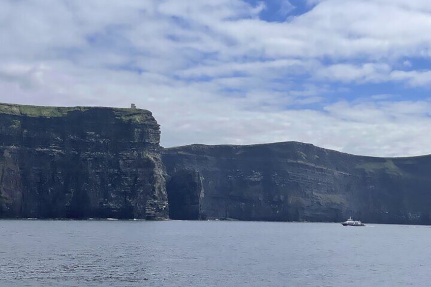 Eine Küstenklippe mit einer kleinen Struktur obenauf und einem Boot im Wasser. 1