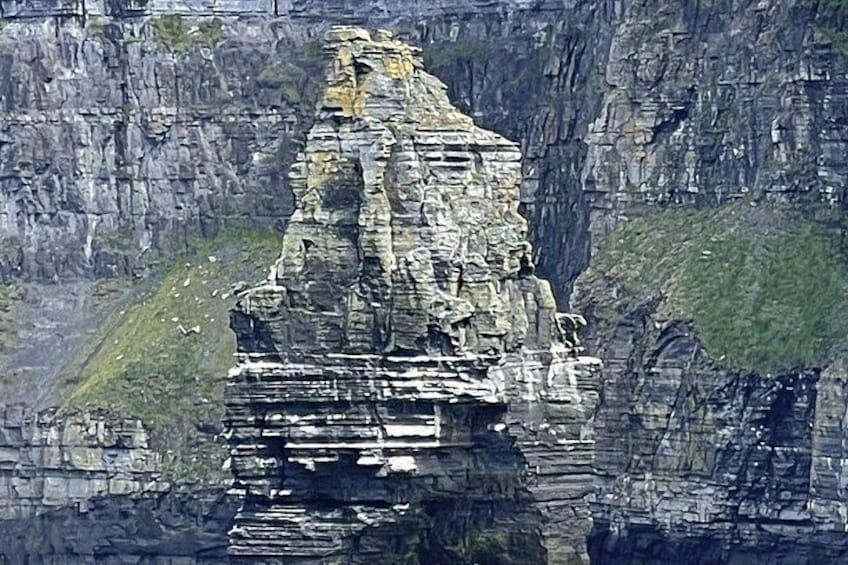 Eine zerklüftete Felsformation mit geschichteten Gesteinsschichten und einer kleinen Grünfläche am Fuße. 5