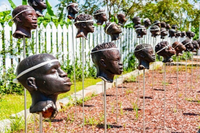 A row of head sculptures in an outdoor setting with a white picket fence in the background. 1