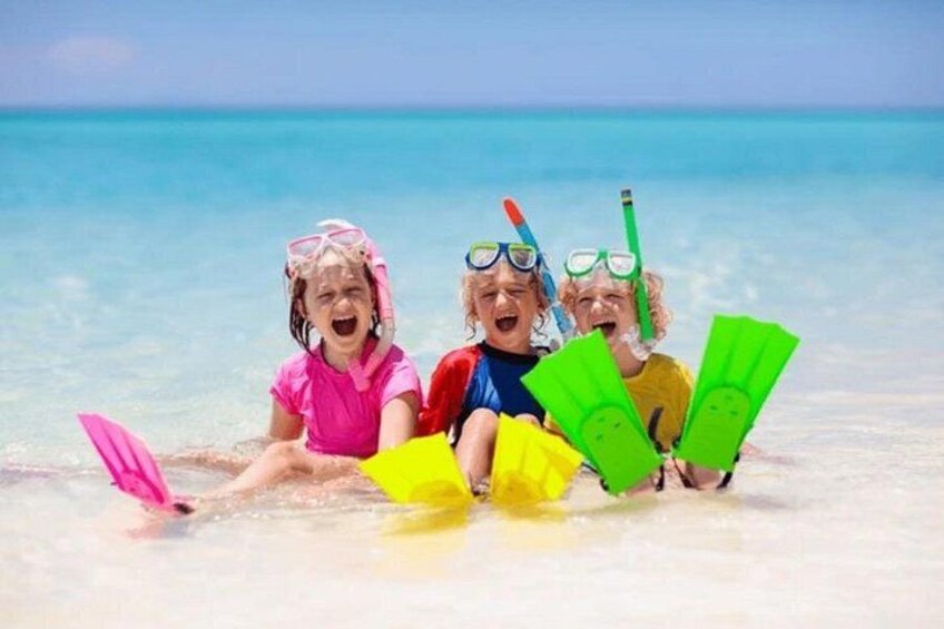 Three children snorkeling on a beach with clear blue water. 2