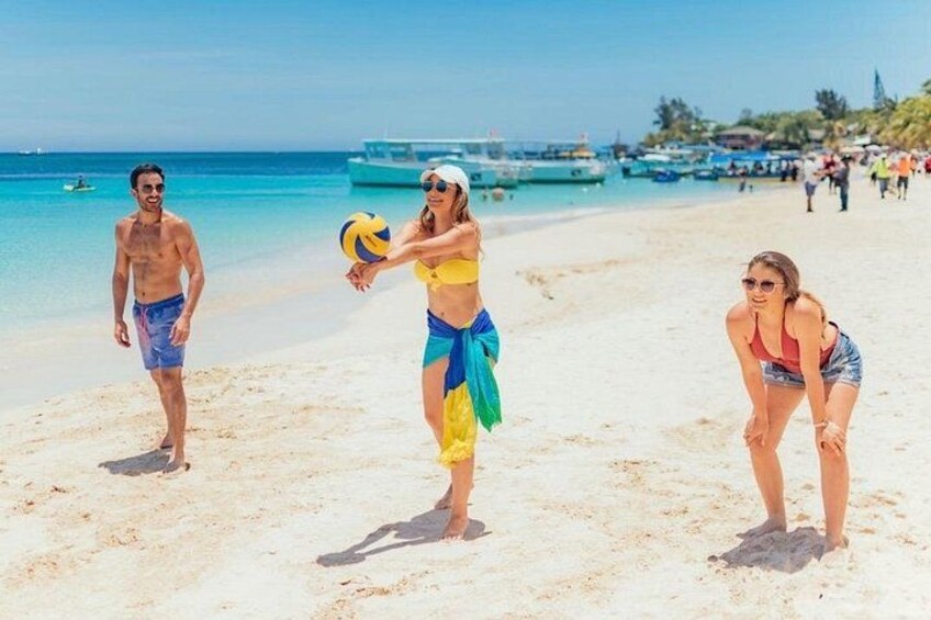 Ein Strand mit Menschen, die Volleyball spielen, ein Boot im Wasser und einem klaren Himmel. 5