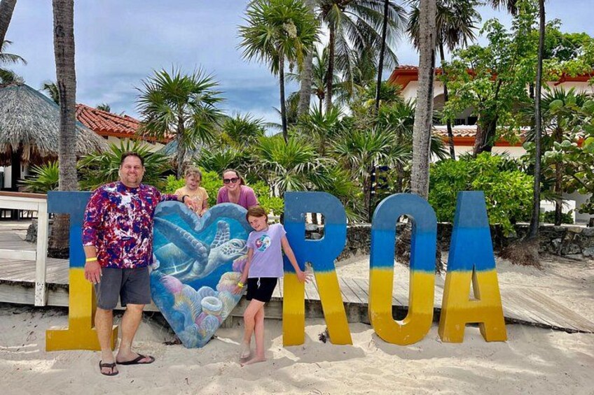 A family posing in front of a large sign with the word 'TOHORA' and a mural of a sea turtle. 3