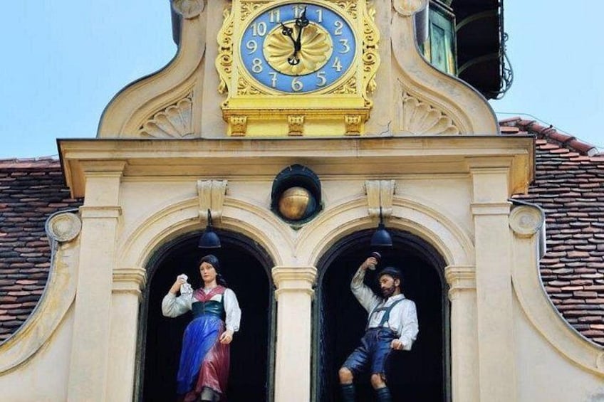 Un campanile con due statue, una raffigurante una donna e una un uomo, e un edificio con tetto in tegole. 3
