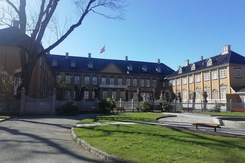 Een groot, historisch gebouw met een symmetrische gevel, een vlag en een verzorgd gazon. 3