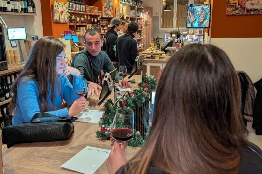 Folk smager på vin i en hyggelig bar med et godt udvalg og et festligt juletræ. 1