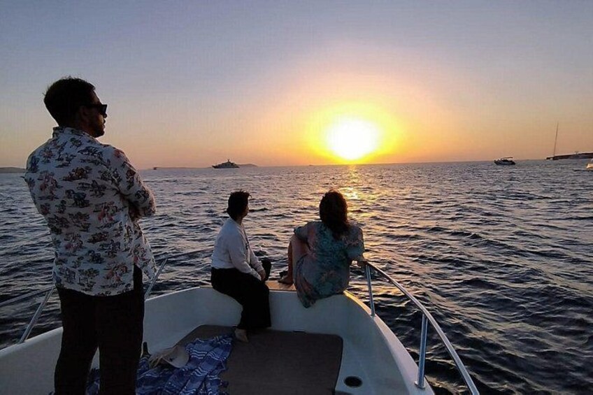 A boat with three people at sunset, calm sea, distant boats, and a clear sky. 3