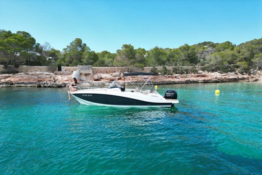 A boat on clear turquoise water with a rocky shoreline and trees in the background. 2