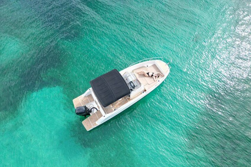 A small boat with a canopy, motor, and seating on a turquoise sea. 3