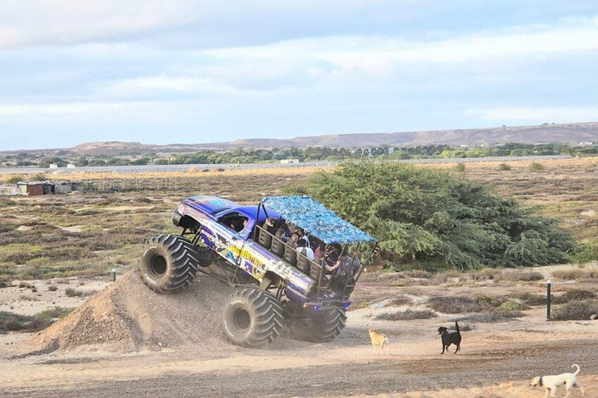 A monster truck driving on a dirt road with a group of people on board. 2