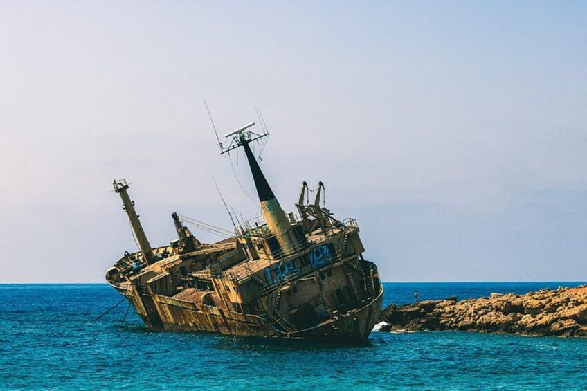 A sunken shipwreck in clear blue waters near a rocky shore. 2