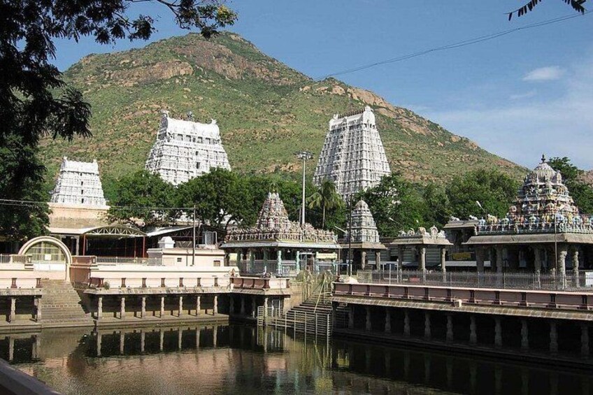 A temple complex with multiple shrines, a large hill in the background, and a calm water body in the foreground. 2