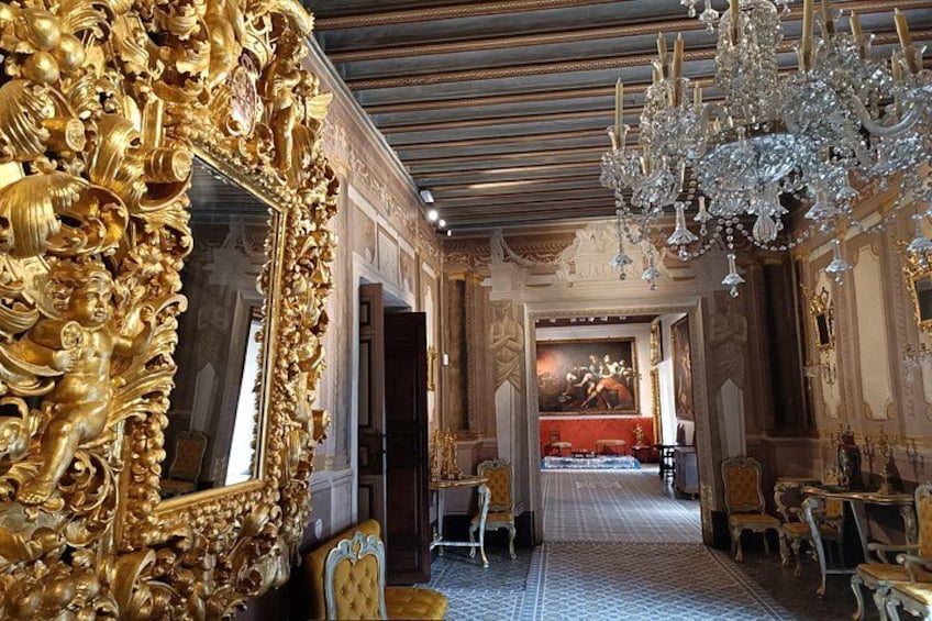 An ornate room with a large golden mirror, a chandelier, and a red carpet. 2