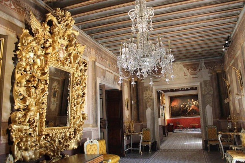 An opulent room with a large ornate gold mirror, a chandelier, and classical architecture. 1