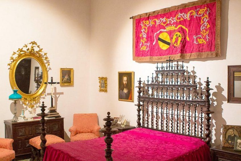 A bedroom with a bed, a mirror, a cross, and a tapestry. 3