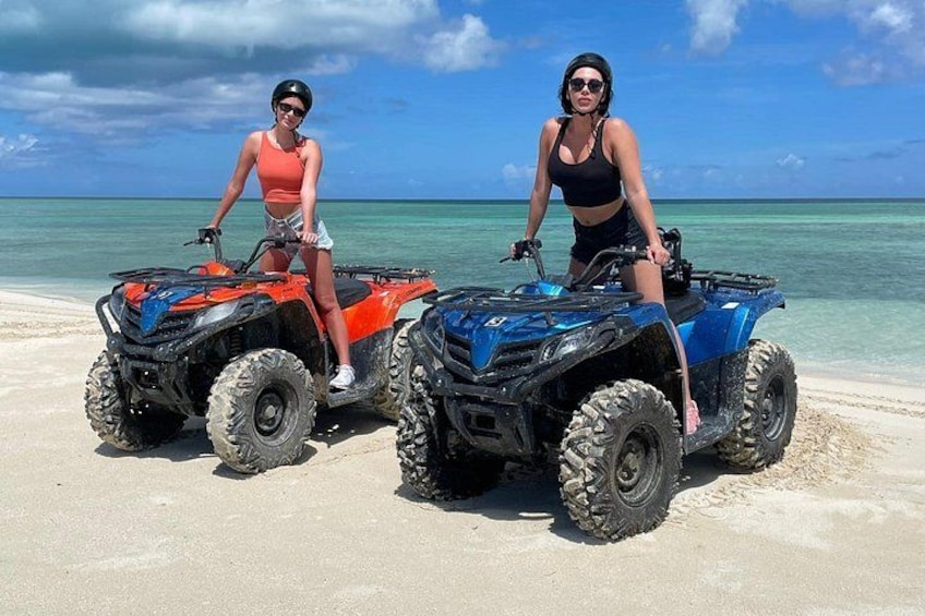 To ATV'er på en sandstrand med klart, blåt vand i baggrunden. 1