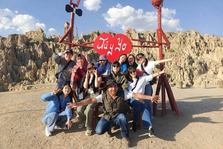 A group of people posing in front of a red structure with a heart-shaped sign that reads 'Judy Yo' in a desert landscape. 2