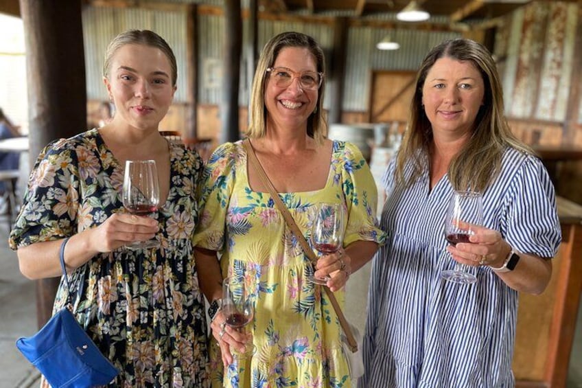 Three people holding wine glasses in a rustic setting with wooden beams and a metal roof. 1