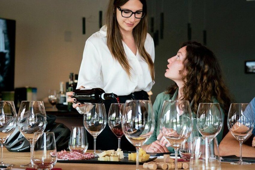 Iemand giet een drankje in een glas, een tafel met verschillende wijnglazen en een fles wijn. 4