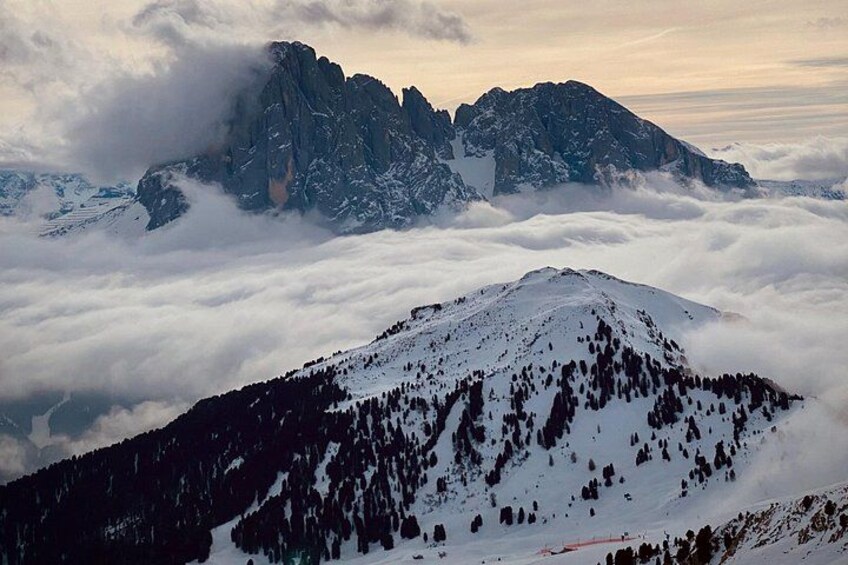 Una cima montuosa innevata con pendii boscosi e una valle coperta di nuvole sotto. 4