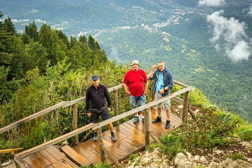 Tre persone in piedi su una piattaforma di legno con una vista panoramica su un paesaggio montuoso. 2