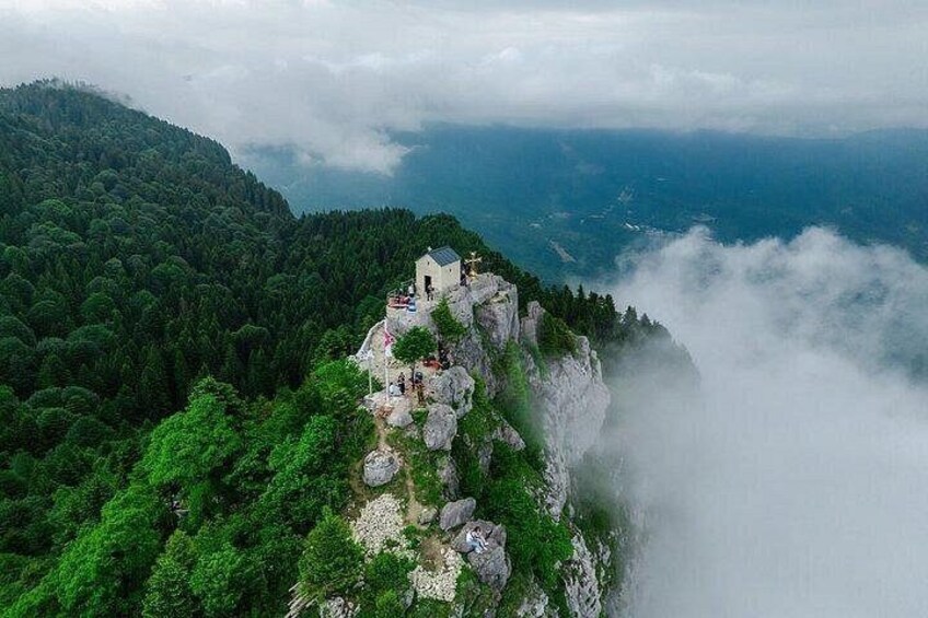 Una vetta montuosa con un piccolo edificio, una rigogliosa foresta verde e nuvole avvolte nella nebbia. 1