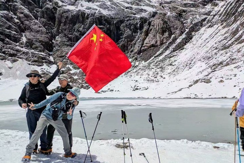 Un grupo de personas en un paisaje nevado con un lago helado, sosteniendo una bandera roja con un emblema amarillo. 4