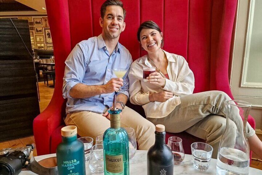 Dos personas sentadas en un sofá rojo con bebidas y botellas sobre una mesa. 2