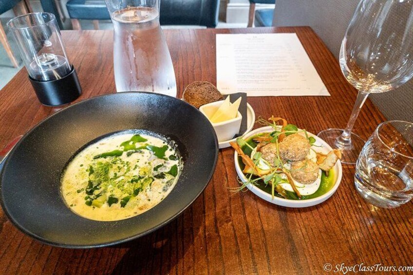 Una mesa de comedor con un tazón de sopa, un plato de ensalada y un vaso de agua. 1