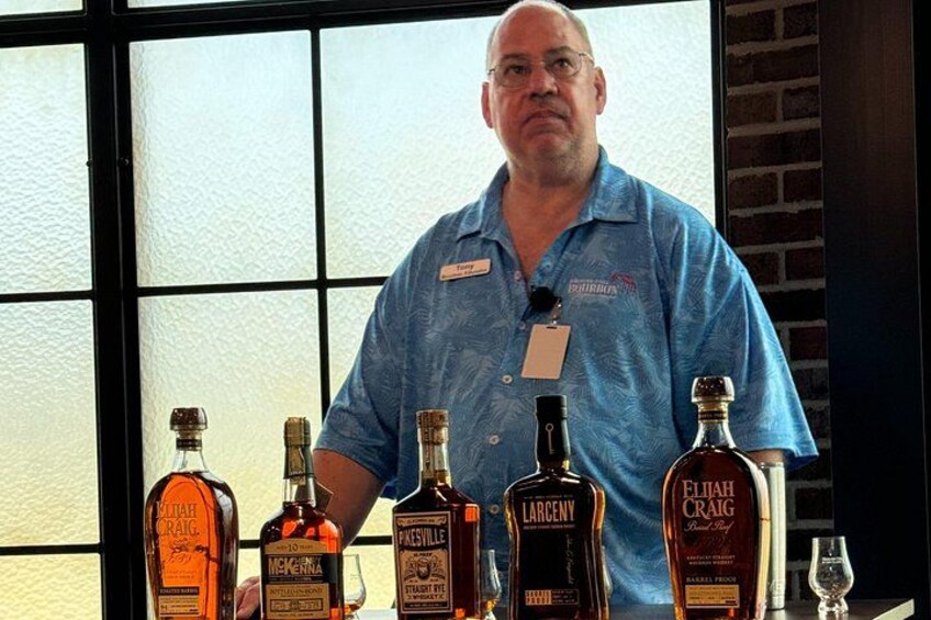 A man standing behind a table with various liquor bottles. 3